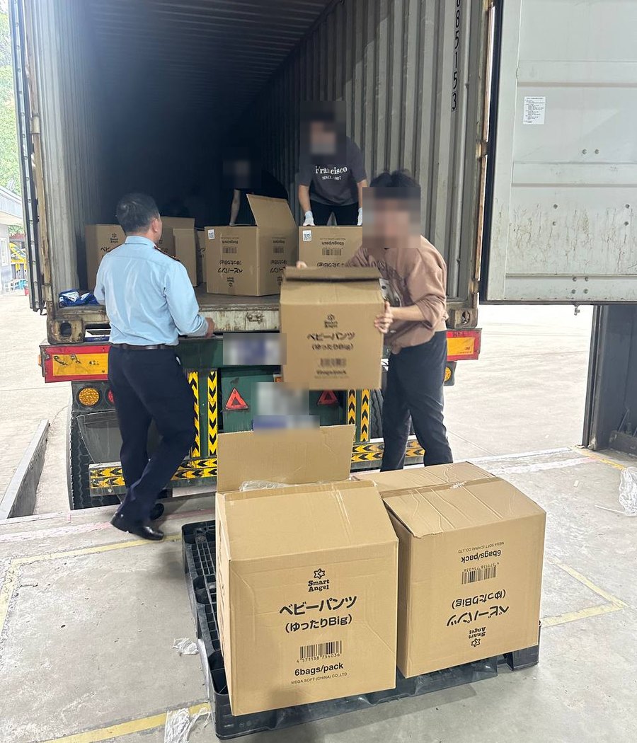 Nhân viên kho dỡ các thùng carton từ container xuống pallet nhựa tại cửa kho, mặt người và biển số xe đã được làm mờ